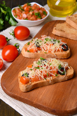 Delicious bruschetta with tomatoes on cutting board close-up
