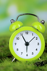 Green alarm clock on grass on natural background