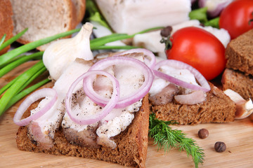 Slices of bread and lard with vegetables on table close up