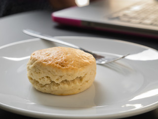 Scone on a white plate and laptop computer