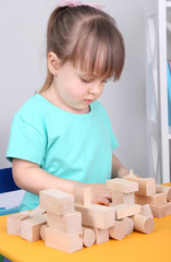 Little girl plays with construction blocks sitting at table in