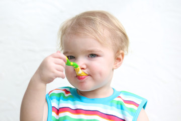 toddler girl wearing colorful bib eating porridge with spoon 
