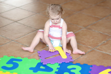 Fototapeta premium Happy toddler girl playing with colorful numbers puzzles