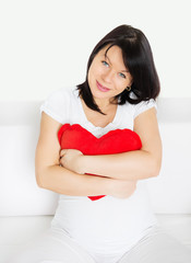 Beautiful,pregnant woman holding a heart shape pillow and looking at camera