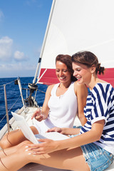 Happy women on the bow of a Sailboat using a laptop