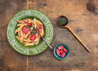 Penne pasta tuna sauce, tomatoes in green plate,old wooden table