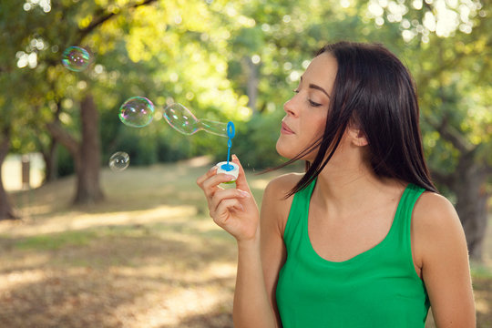 Beautiful young woman blowing soap bubbles outdoors