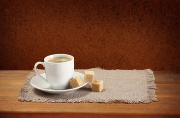 Coffee cup, saucer, sugar, napkin on wooden table.