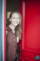 beautiful young woman opening a red door to welcome someone