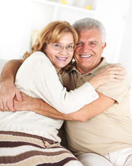 Hugging Senior couple sitting in living room.