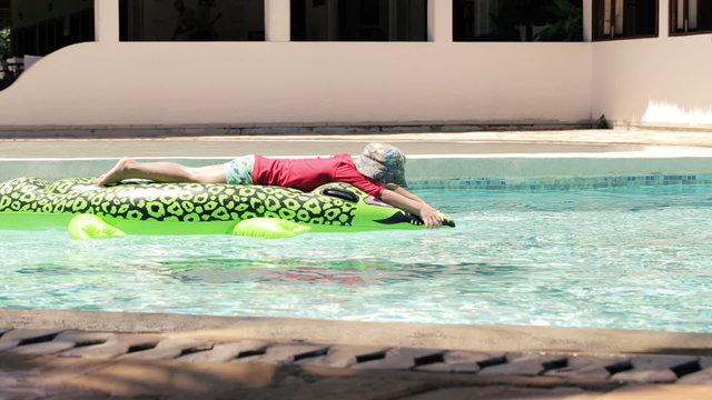 Young cute boy swimming on crocodile shaped mattress in swimming