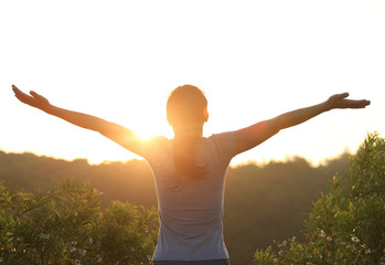 cheering woman open arms at sunrise mountain peak