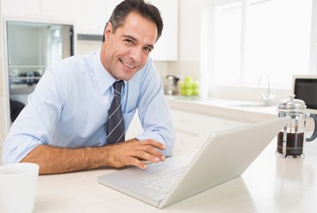 Fototapeta na wymiar Smiling well dressed man using laptop in kitchen