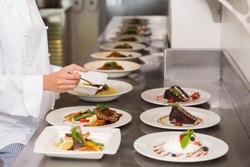 Mid section of a female chef garnishing food in kitchen
