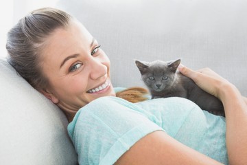 Cheerful woman lying on sofa cuddling a grey kitten