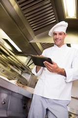 Naklejka na ściany i meble Smiling male cook using digital tablet in kitchen