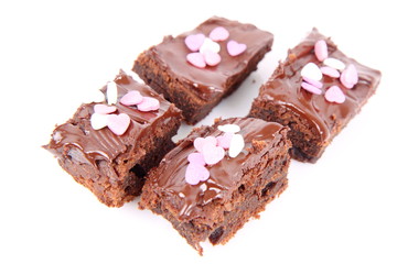 Slices of a brownie covered with chocolate and decorated with sugar hearts