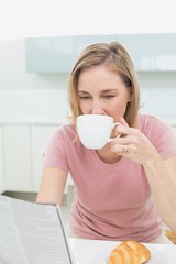 Woman reading newspaper while having coffee in kitchen