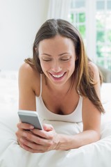 Smiling woman text messaging in bed