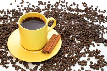 Yellow cup of coffee with cinnamon and spilled coffee beans