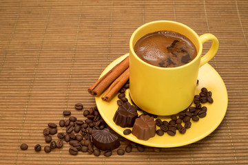 Yellow cup of coffee with cinnamon,candies and coffee beans
