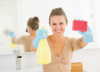 Happy young housewife showing spray bottle and sponge