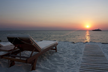 empty sun lounger at sunset on beach with boat