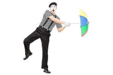 Mime artist holding an umbrella simulating being blown by wind