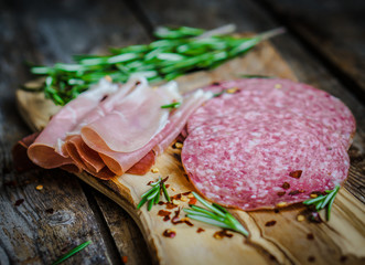 Sliced prosciutto di Parma on wooden board with salami and rosem