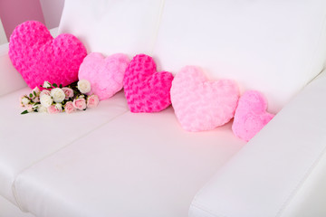 Pink hearts shaped pillow and flowers on white sofa