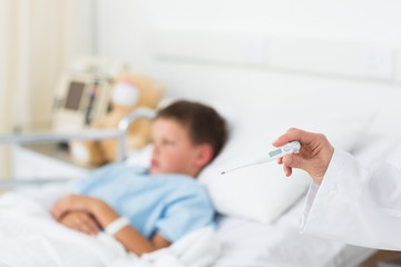 Fototapeta premium Doctor holding thermometer with boy in hospital