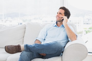 Cheerful man sitting on the couch making a phone call
