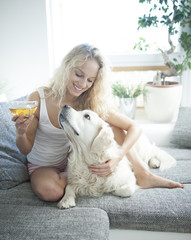 Beautiful woman holding tea cup while touching dog on sofa