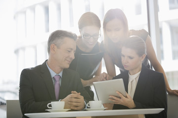 Business people using digital tablet together in office cafeteria
