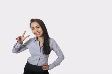 Portrait of happy businesswoman showing victory sign against gray background
