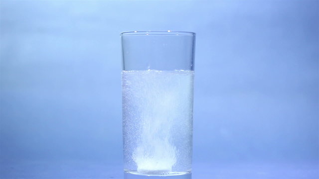 Tablet of sparkling aspirin in glass on  blue background