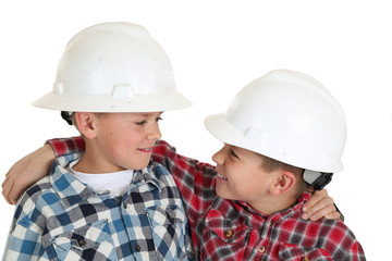 Two boys hugging wearing construction hardhats smiling