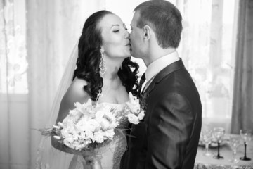 Black and white portrait of bride and groom kissing at home