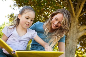 Happy mother and daughter reading a book at park