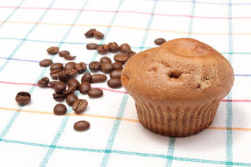 Fresh baked muffin and coffee grains on colorful cloth