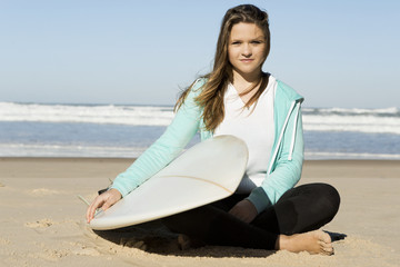 Fototapeta na wymiar Teenage surfer girl sitting in the beach with her surfboard