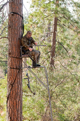 Bow hunter in a ladder style tree stand safely raising his bow with a haul line