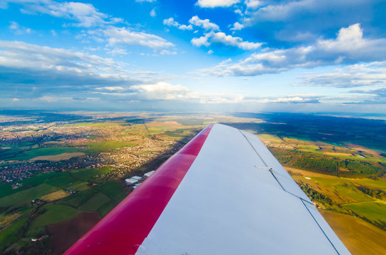 Fototapeta Aerial view of a plane wing flying over green fields
