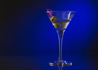 wineglass with martini and olives on blue background.