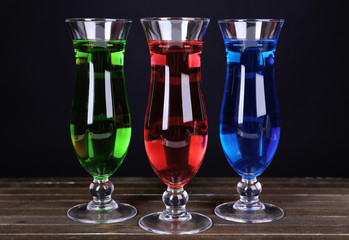 Glasses of cocktails on table on black background