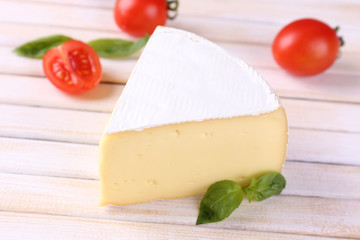 Tasty Camembert cheese with basil and tomatoes, on wooden table