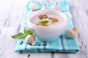 Mushroom soup in white pot, on napkin,  on wooden background