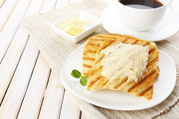 Grilled bread with butter and cup of coffee on wooden table