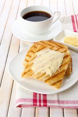 Grilled bread with butter and cup of coffee on wooden table