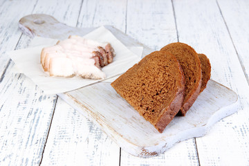 Slices of bread and lard on cutting board on wooden background